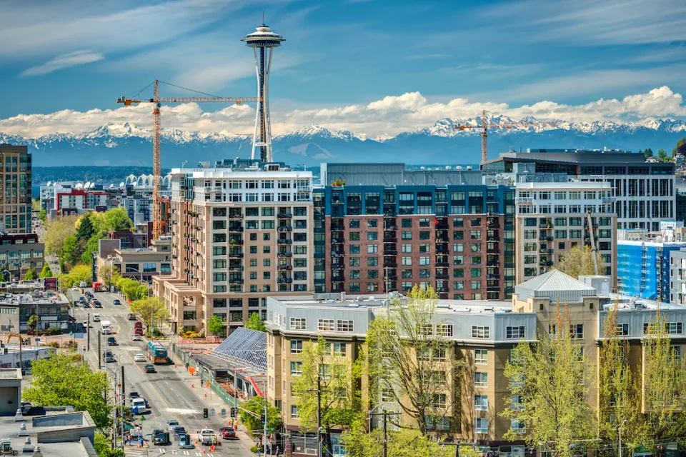 View of multistory buildings under construction in downtown Seattle, Washington with Space Needle and Mount Rainier in background.